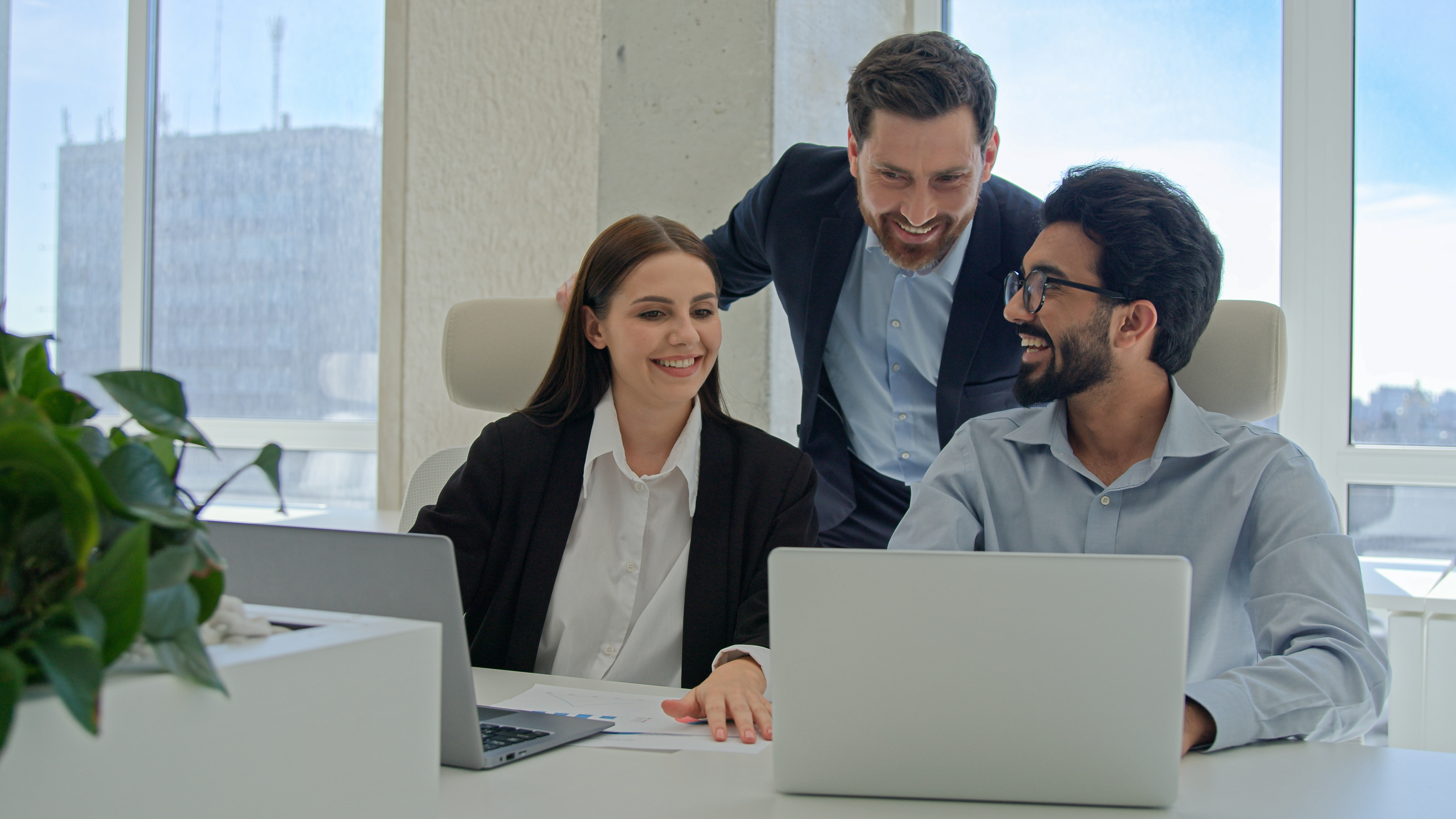 drei lachende Personen in Business-Kleidung arbeiten an PC.