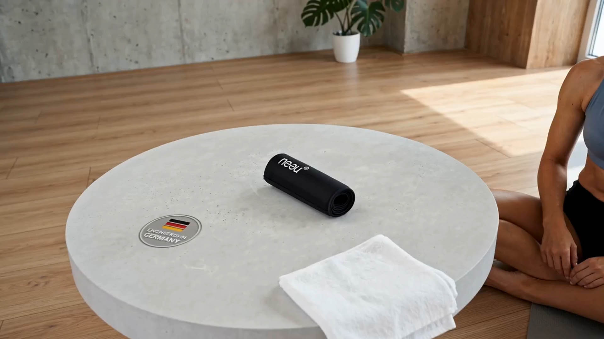 Das neeu Kühlpad und ein Handtuch liegen auf einem Wohnzimmertisch neben einer sitzenden Frau in Sportkleidung